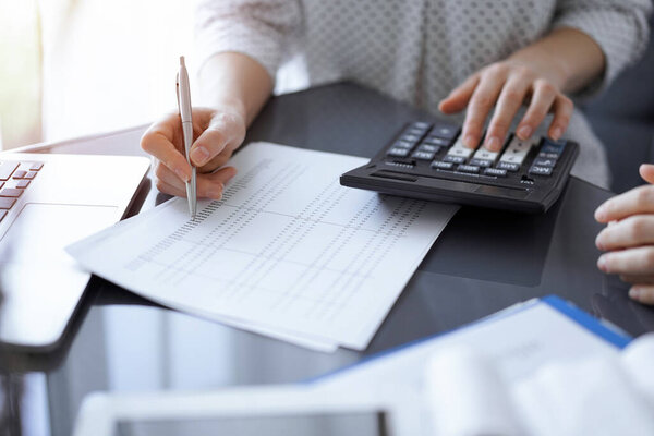 Женщина-бухгалтер с помощью калькулятора и ноутбука при подсчете налогов для клиента. Концепции бизнес-аудита.