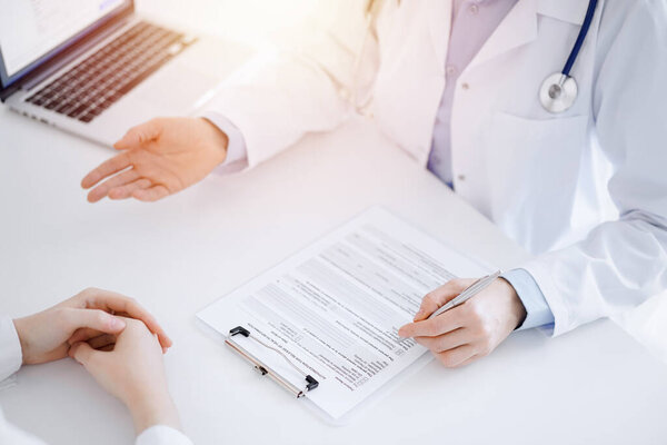 Doctor and patient discussing current health questions while sitting opposite of each other and using clipboard at the table in clinic, just hands closeup. Medicine concept.