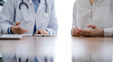 Doktor ve hasta klinikteki ahşap masada yan yana oturuyorlar. Kadın doktorlar kayıt formunu dolduruyorlar. Tıp konsepti.