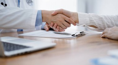 Doktor ve hasta klinikteki ahşap masanın üstünde el sıkışıyor. Tıp konsepti.