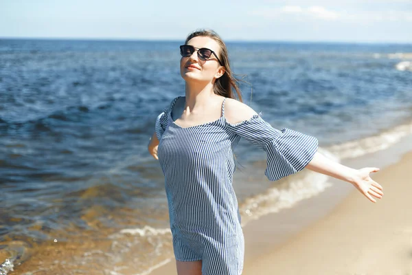 Okyanus sahilinde mutlu, mutlu ve mutlu bir kadın elleri açık duruyor. Yazlık elbiseli esmer bir kadın modelin portresi. Gezici tatiller sırasında doğanın tadını çıkarıyor..
