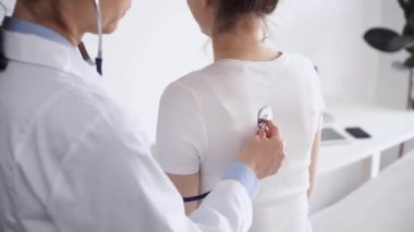 Doktor ve hasta klinikte olağan sağlık kontrolündeler. Terapist, genç bir kadını steteskopla muayene ediyor. Tıp konsepti.