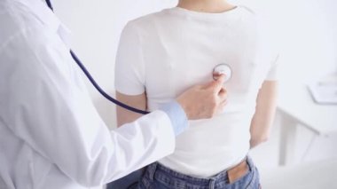Doktor ve hasta klinikte olağan sağlık kontrolündeler. Terapist, genç bir kadını steteskopla muayene ediyor. Tıp konsepti.