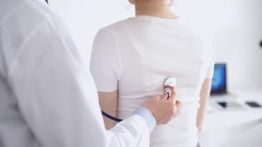 Doktor ve hasta klinikte olağan sağlık kontrolündeler. Terapist, genç bir kadını steteskopla muayene ediyor. Tıp konsepti.