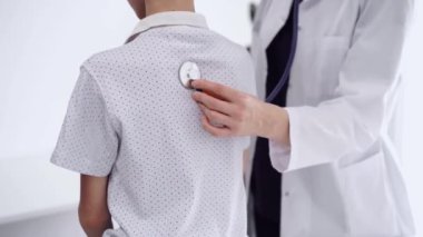 Doktor ve çocuk hasta klinikte. Beyaz önlüklü bir doktor steteskopla genç bir çocuğu muayene ediyor. İlaç, terapi konsepti.