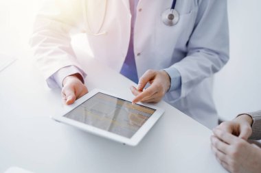 Doktor ve hasta klinikteki masada oturuyor. Tablet bilgisayar kullanan kadın doktorların ellerine odaklan, kapat. Tıp ve sağlık hizmetleri kavramı.