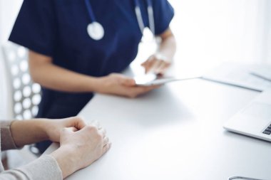 Doktor ve hasta bir şey tartışıp tablet bilgisayar kullanırken klinikteki masada oturuyorlar. Kadın hastaların ellerine odaklan, kapat. Tıp konsepti.