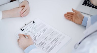 Doktor ve hasta birbirlerine karşı otururken sağlık sorularını tartışıyorlar ve klinikteki masada pano kullanıyorlar, sadece elleri yakın çekim. Tıp konsepti.