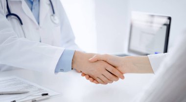 Klinikteki masada karşılıklı otururken doktor ve hasta el sıkışıyor. Sadece eller kapalı. Tıp konsepti.