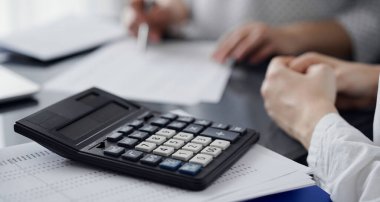 Müşteri ile vergi sayarken ve tartışırken kalem ve dizüstü bilgisayar kullanan kadın muhasebeci, hesap makinesine odaklan. İş denetimi ve finans kavramları.