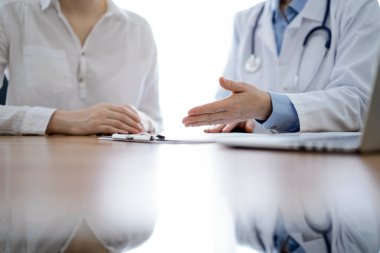 Doktor ve hasta, klinikteki ahşap masada yan yana otururken bir şey tartışıyorlar. Tıp konsepti.