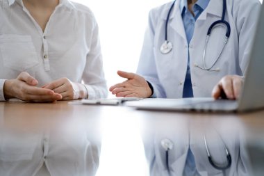 Doktor ve hasta laptoplarını kullanırken ve klinikteki ahşap masada yan yana otururken bir şeyler tartışıyorlar. Tıp konsepti.