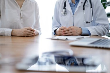 Doktor ve hasta, klinikteki ahşap masada yan yana otururken ellerini kapatarak bir şey tartışıyorlar. Tıp konsepti.