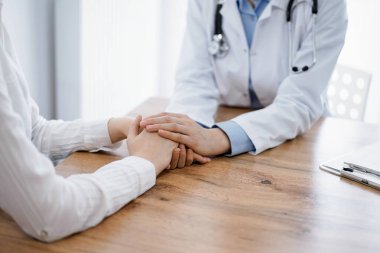 Doktor ve hasta klinikteki ahşap masada oturuyorlar. Kadın doktorların elleri güven veren kadınlarındır. Tıp konsepti.