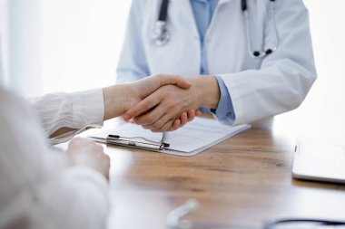 Doktor ve hasta klinikteki ahşap masanın üstünde el sıkışıyor. Tıp konsepti.