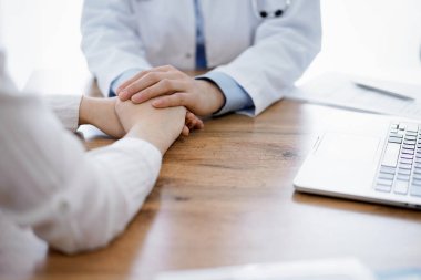 Doktor ve hasta klinikteki ahşap masada oturuyorlar. Kadın doktorların elleri güven veren kadınlarındır. Tıp konsepti.