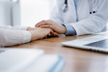 Doktor ve hasta klinikteki ahşap masada oturuyorlar. Kadın doktorların elleri güven veren kadınlarındır. Tıp konsepti.