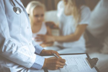 Doktor ve hasta. Pediyatrist, annesiyle birlikte küçük kızı muayene ederken pano kullanıyor. Sağlık muayenesinde mutlu beyaz çocuk. Tıp konsepti.