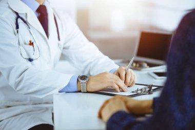Bir doktor, hastanedeki güneşli dolapta birlikte otururken hastasıyla konuşuyor. Doktor ilaç kayıtlarını doldurmak için pano kullanıyor. Mükemmel tıbbi servis.