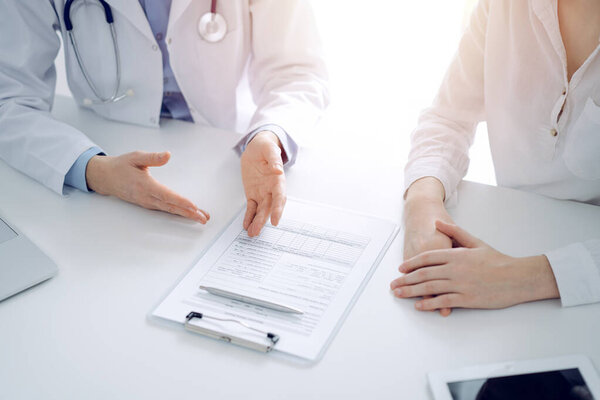 Doctor and patient discussing current health questions while sitting near of each other and using clipboard at the table in clinic, just hands closeup. Medicine concept.