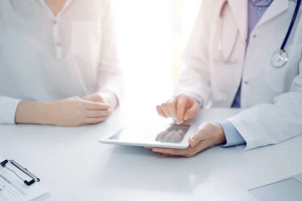 stock image Doctor and patient sitting near each other at the desk in clinic. The focus is on female physicians hands pointing into tablet computer touchpad, close up. Medicine concept.