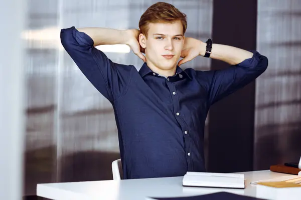 Young blond businessman and programmer stretching hands after working hard with computer. Startup business leads to success.