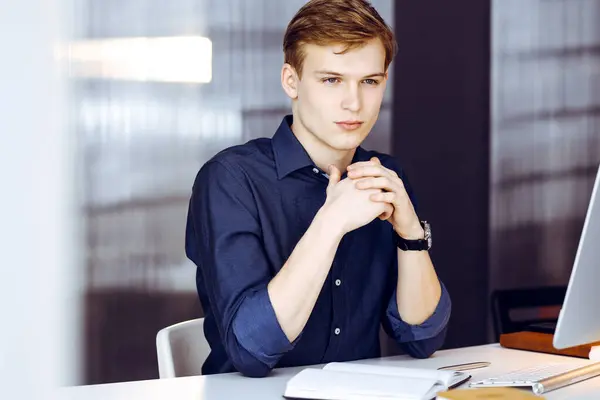 Young blond businessman thinking about strategy at his working place with computer. Startup business means working hard and out of time for success achievement.