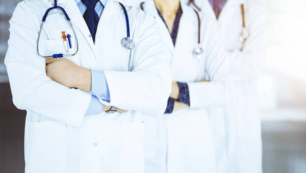 Group of modern doctors standing as a team with crossed arms and stethoscopes in a sunny hospital office. Physicians ready to examine and help patients.