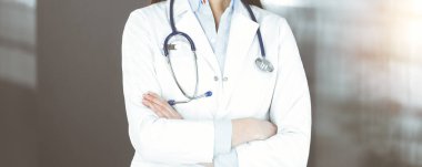 Kimliği belirsiz genç bir kadın doktor güneşli klinikte kollarını kavuşturmuş duruyor. Coronavirus salgını sırasında ilaç konsepti. Covid 2019.