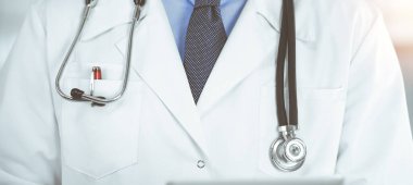 Bilinmeyen erkek doktor, güneşli klinikte dururken elinde tablet bilgisayar kullanıyordu. Coronavirus salgını sırasında ilaç konsepti. Covid 2019.