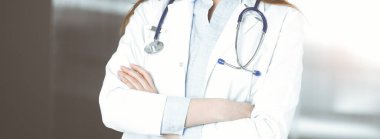 Kimliği belirsiz genç bir kadın doktor güneşli klinikte kollarını kavuşturmuş duruyor. Coronavirus salgını sırasında ilaç konsepti. Covid 2019.