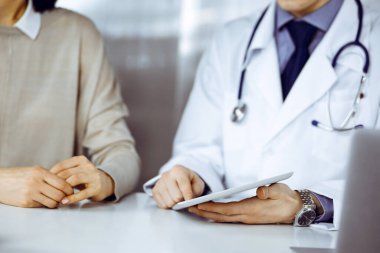 Bilinmeyen erkek doktor ve hasta kadın klinikte oturup tablet bilgisayar kullanırken bir şeyler tartışıyorlar. Hastanedeki en iyi sağlık hizmeti, ilaç, salgın durdurma..