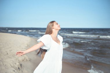Mutlu gülümseyen güzel kadın okyanus sahilinde beyaz bir yaz elbisesi içinde, kolları açık..