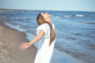 Mutlu gülümseyen güzel kadın okyanus sahilinde beyaz bir yaz elbisesi içinde, kolları açık..