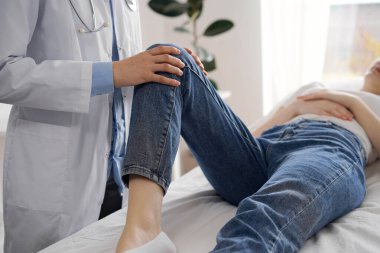 Doktor ve hasta klinikte olağan sağlık kontrolündeler. Terapist genç bir kadının dizini muayene ediyor. Tıp konsepti .