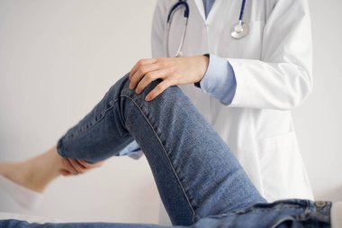 Doktor ve hasta klinikte olağan sağlık kontrolündeler. Terapist genç bir kadının dizini muayene ediyor. Tıp konsepti .