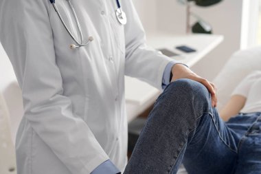 Doktor ve hasta klinikte olağan sağlık kontrolündeler. Terapist genç bir kadının dizini muayene ediyor. Tıp konsepti .