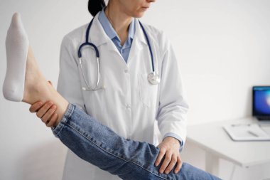 Doktor ve hasta klinikte olağan sağlık kontrolündeler. Terapist genç bir kadının dizini muayene ediyor. Tıp konsepti .