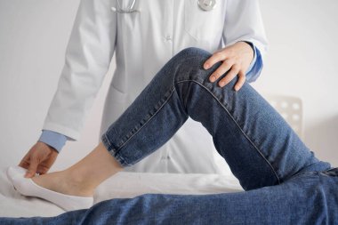 Doktor ve hasta klinikte olağan sağlık kontrolündeler. Terapist genç bir kadının dizini muayene ediyor. Tıp konsepti .