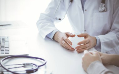 Doktor ve hasta klinikteki masada otururken güncel sağlık sorularını tartışıyorlar, sadece eller kapalı. Tıp konsepti.