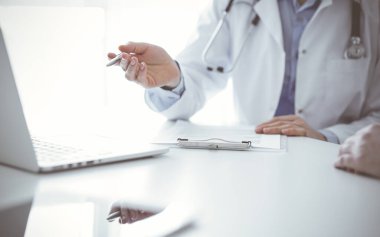 Doktor ve hasta klinikteki masada oturuyor. Diz üstü bilgisayar monitörünü işaret eden kadın doktorlara odaklanıyoruz, kapatın. Tıp konsepti.