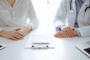 Doktor ve hasta birbirlerine yakın otururken sağlık sorularını tartışıyorlar ve klinikteki masada pano kullanıyorlar, sadece ellerini kapatıyorlar. Tıp konsepti.