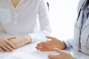 Doktor ve hasta birbirlerine yakın otururken sağlık sorularını tartışıyorlar ve klinikteki masada pano kullanıyorlar, sadece ellerini kapatıyorlar. Tıp konsepti.