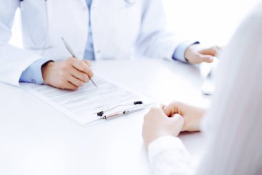 Doktor ve hasta bir şey tartışıyor ve klinikteki masada karşılıklı otururken dizüstü bilgisayar kullanıyorlar. Mükemmel tıbbi hizmet ve tıp konsepti.