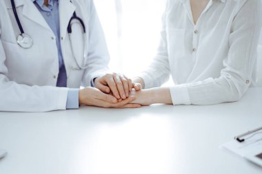 Doktor ve hasta klinikteki masada yan yana oturuyorlar. Kadın doktorlara odaklan. Kadına güven veren eller, sadece eller, yakın çekim. Tıp konsepti.