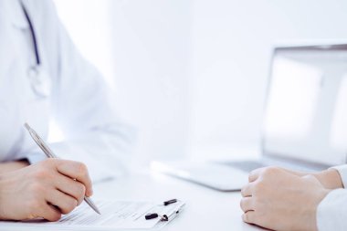 Doktor ve hasta klinikteki masada karşılıklı oturuyorlar. Kadın doktorların ellerinin tıbbi geçmiş kayıtlarını doldurması ya da kontrol listesi üzerinde yoğunlaşacağız. Kapat. Tıp konsepti.