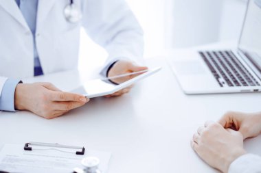 Doktor ve hastanın önünde duran steteskop arka planda tablet bilgisayar kullanıyordu. Tıp, sağlık hizmeti kavramı.