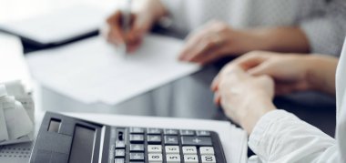 Müşteri ile vergi sayarken ve tartışırken kalem ve dizüstü bilgisayar kullanan kadın muhasebeci, hesap makinesine odaklan. İş denetimi ve finans kavramları.