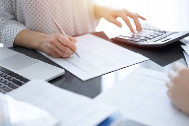 Müşteri ya da meslektaşıyla birlikte vergi sayarken hesap makinesi ve dizüstü bilgisayar kullanan kadın muhasebeci. İş denetleme ekibi, finans danışmanı.