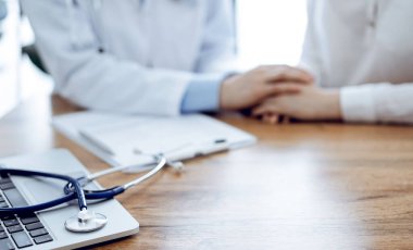 Stetoskop ve dizüstü bilgisayar ahşap masada yatarken doktorlar arka plandaki hastaya güvence veriyor. Tıp konsepti.